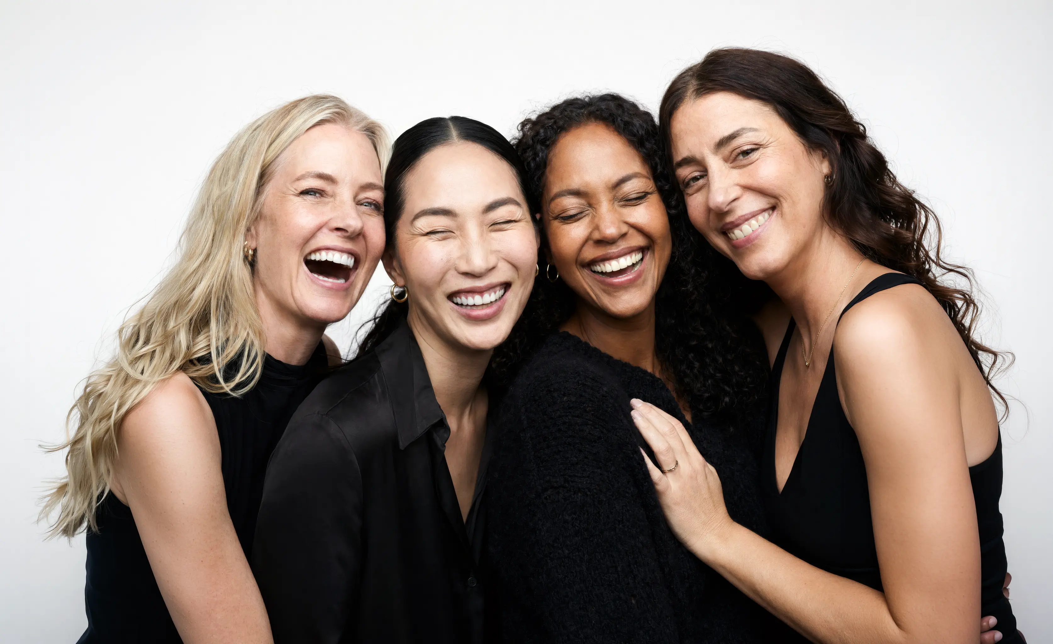 Four women with different skin tones laughing together